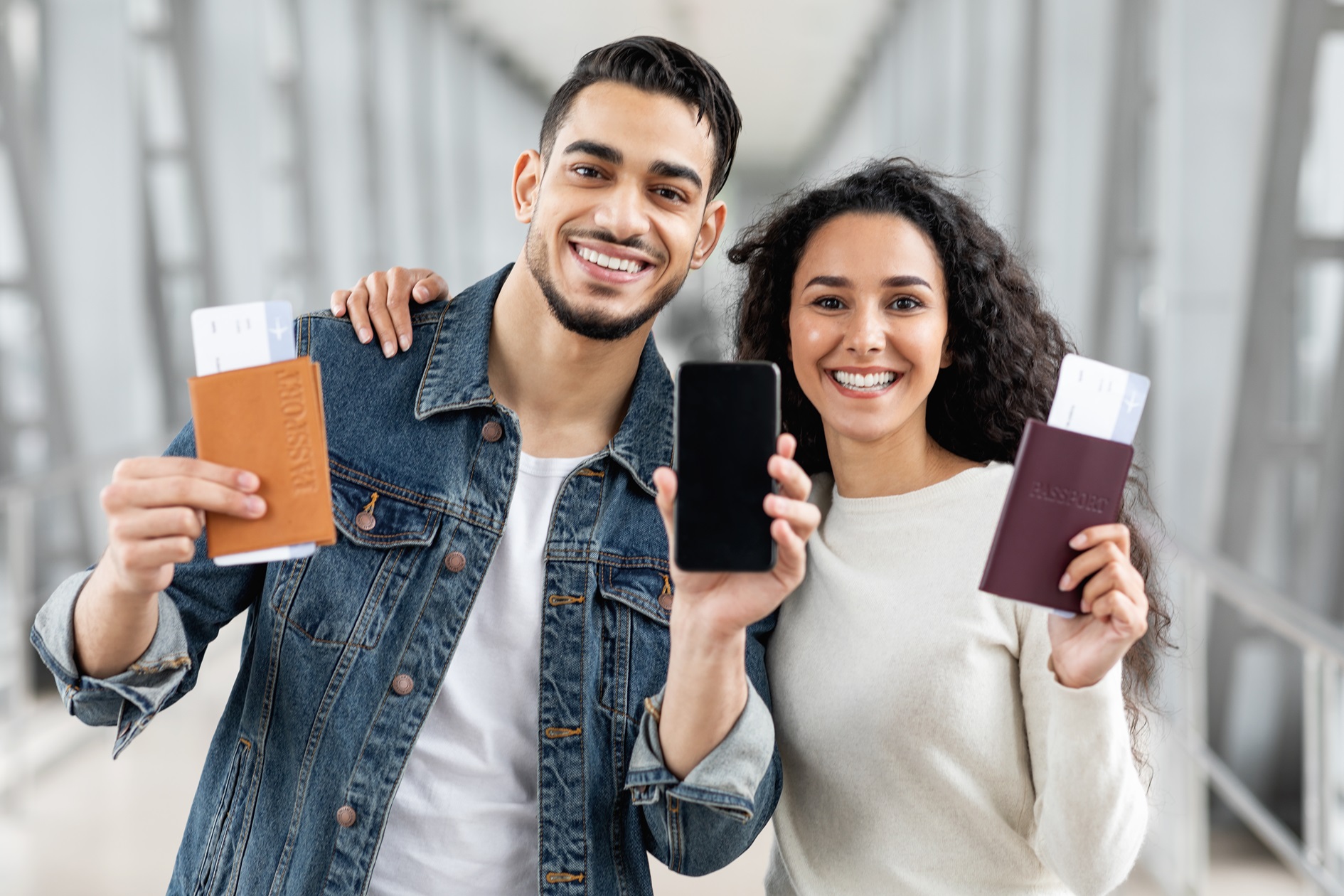 Buy Tickets Online. Arab Couple Standing At Airport And Showing Blank Smartphone