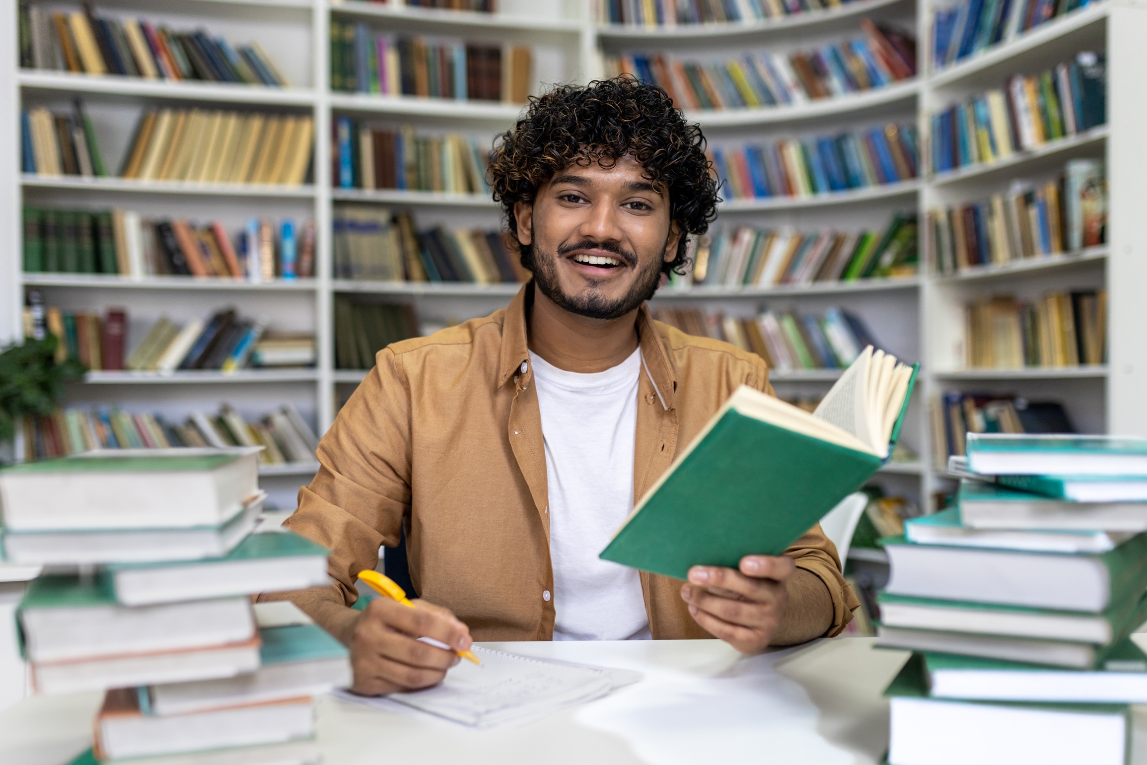 Smiling student studying with books at library in preparation for university exams